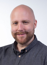 En flintskallig man med bockskägg ler mot kameran.