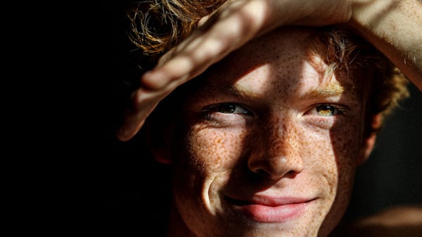 En ung man med fräknigt hår håller händerna över huvudet.