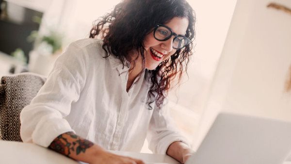 Leende kvinna deltar i distanskurs i programmering vid laptop i hemmiljö