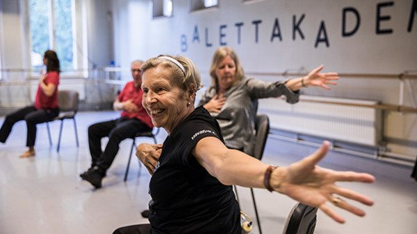 äldre glad kvinna sitter och dansar i danssal på Balettakademien
