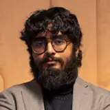 En man med skägg och glasögon som står med armarna i kors.