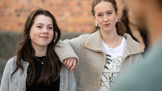 Två studenter som står på skolgården i samspel med en tredje student. 