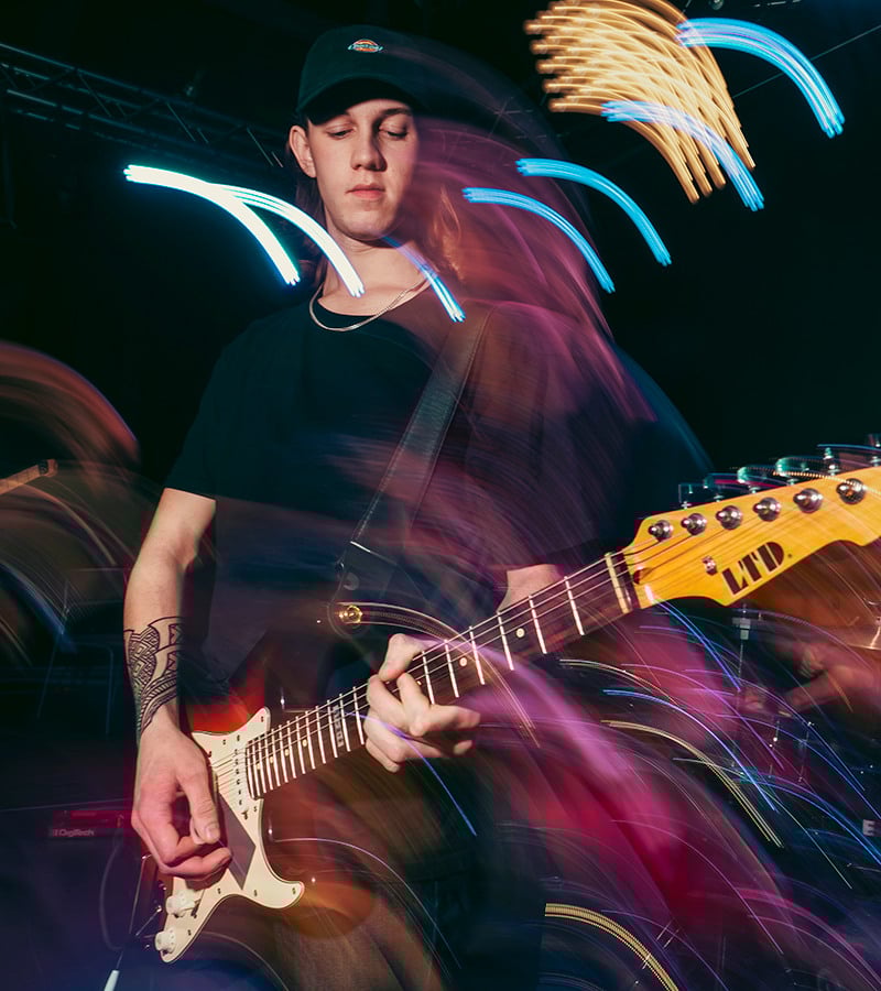 A young man playing electrical guitar on stage.