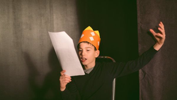 11 years old boy enjoying drama club rehearsal. Holding script and reading.