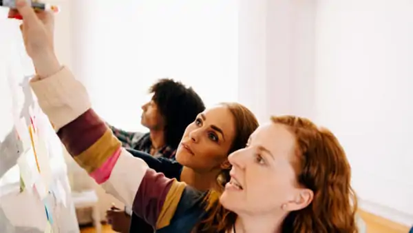 Three people collaborating and writing on a whiteboard