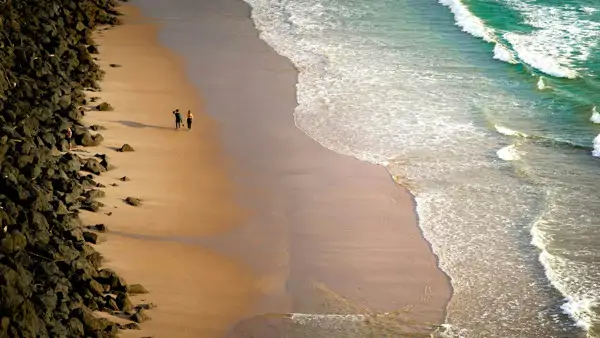 Två personer som promenerar längs en strand vid havet i Biarritz. Åk på språkresa.