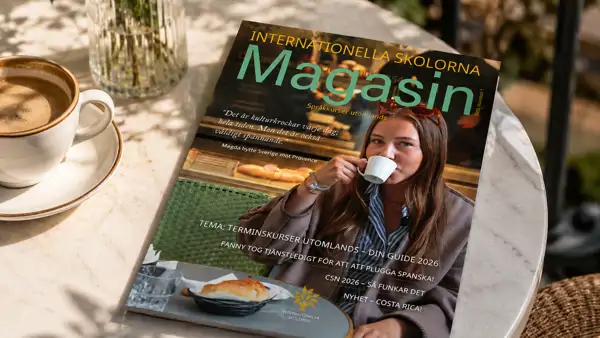 Internationella Skolornas magasin som ligger på ett bord bredvid en kopp kaffe.