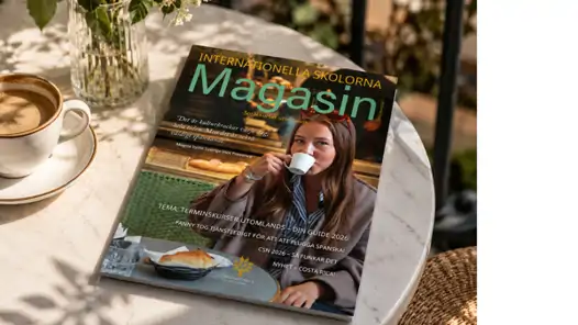 Internationella Skolornas magasin som ligger på ett bord bredvid en kopp kaffe.