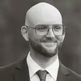 En man med flintskalligt huvud i kostym och slips.