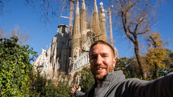 Cheerful young man taking a selfie portrait at the Familia Sagrada in Barcelona, Spain. People traveling fun concept. Shot in winter in a sunny day.