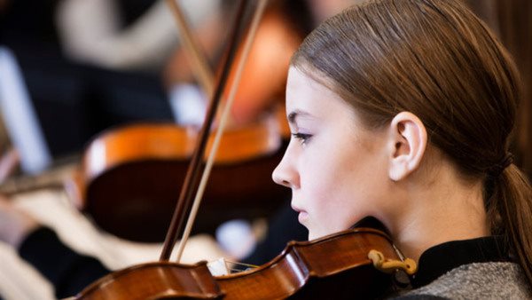 Caucasian girl playing violin in orchestra