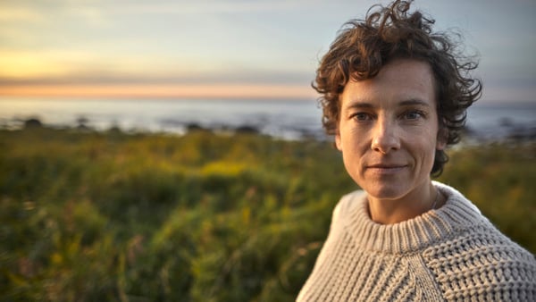 Kvinna som står i högt gräs och tittar in i kameran.