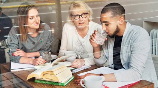 Tre personer som sitter vid ett bord med böcker och pratar