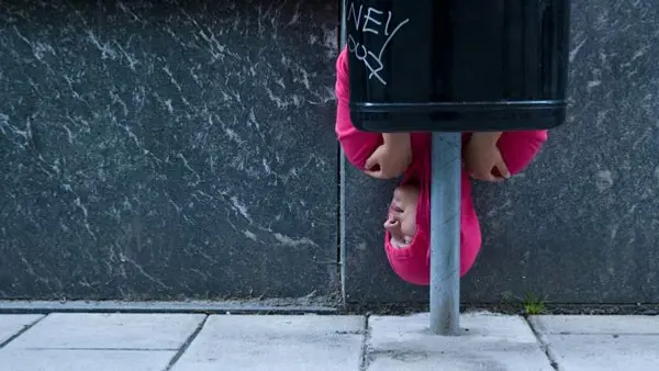 Person i rosa hoodie är uppochner bakom en papperskorg på en trottoar.