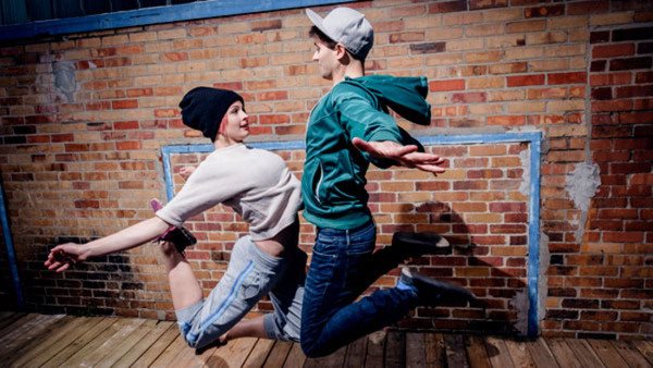 två ungdomar som dansar street möts i ett hopp framför en tegelvägg