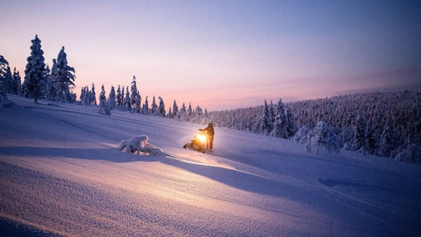 En man åker skoter nedför en snötäckt sluttning.