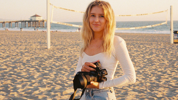 Emma Bahrton står på en strand med en kamera.