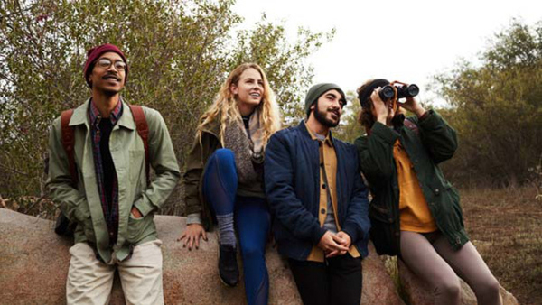 Diverse group of smiling young friends watching something with binoculars while out for a nature hike together