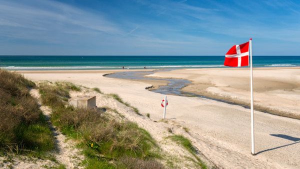 Dansk flagga vajar på en sandstrand vid havet - gå en kurs i danska!