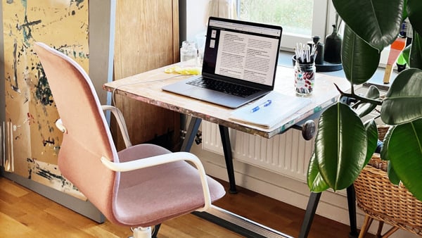 Bild på ett skrivbord med en laptop vid ett fönster.