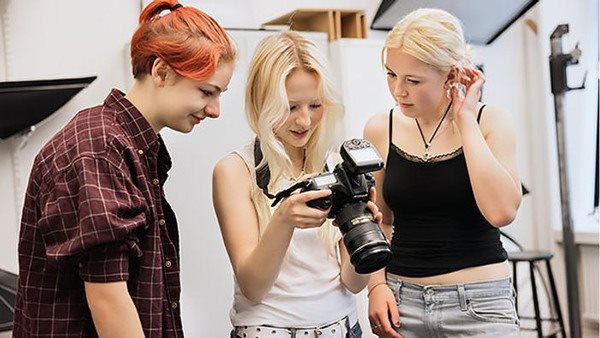 Tre elever på Kungstensgymnasiet står bredvid varandra och tittar på bilder i en kamera.