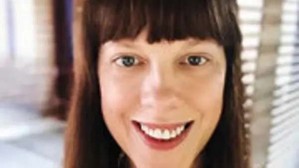 En kvinna med l&aring;ngt brunt h&aring;r som ler mot kameran.