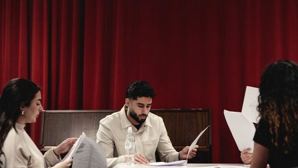 Bild på en ung man och två kvinnor som läser ett manus framför ett rött draperi på Skådespelarlinjen i Husby
