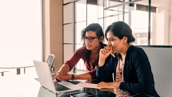 Two women woriking on a laptop in a bright classroom, supporting adult education and inclusion