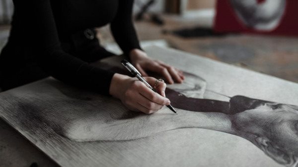 Portrait of young focused Caucasian woman sketching in art studio.