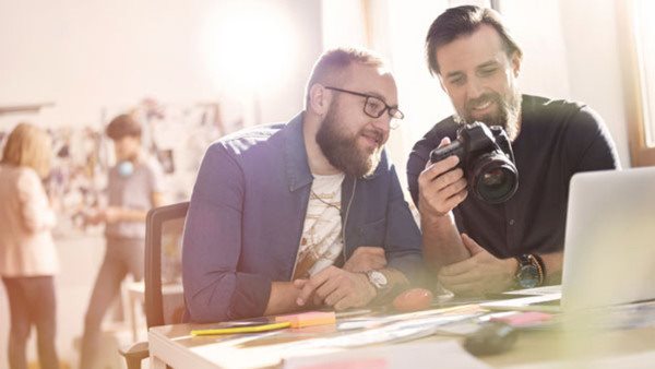 Två grafiska designers granskar bilder på en kamera i en kreativ studiomiljö - praktiskt arbete på designkurs