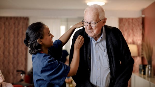 Äldre man får hjälp av vårdpersonal. Båda är glada.