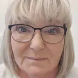 En kvinna med glasögon och vit jacka.