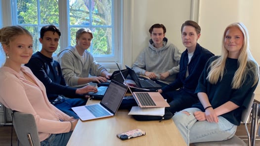 En grupp människor som sitter runt ett bord med bärbara datorer.