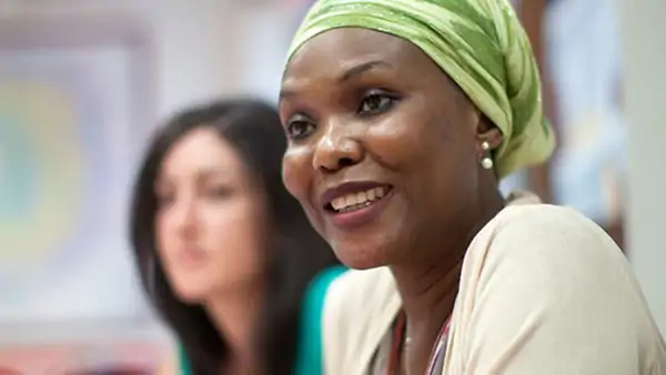 Smiling woman wearing a green headscarf in a classroom, part of the "Korta vägen" program