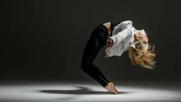 En kvinna i vit skjorta och svarta byxor dansar med kroppen lutande bakåt