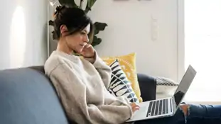En kvinna som sitter i en soffa och använder en bärbar dator.