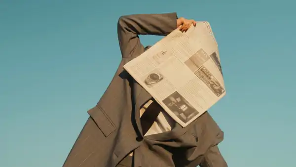 Person i kostym håller en tidning framför ansiktet.