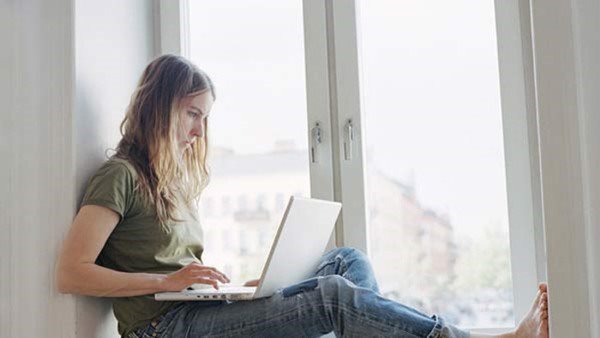Flicka sitter med laptop i en fönsternisch