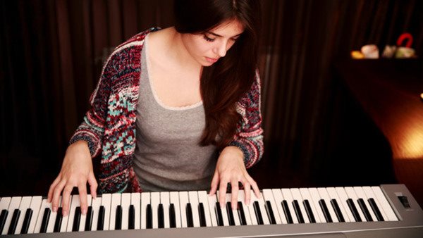 Young beautiful woman playing on piano at home