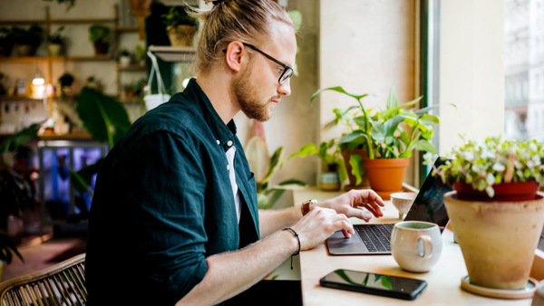 Man sitter med laptop på en solig balkong, i en avslappnad miljö som passar för distansstudier.