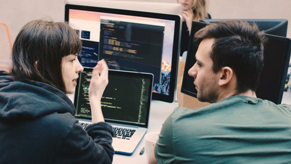 Två deltagare diskuterar kod under en kurs i webbutveckling i klassrumsmiljö