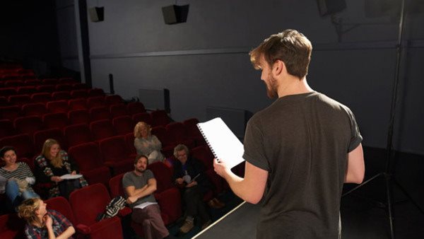 Svartklädd skådespelare med manus i hand på scen - gå en teaterkurs hos Folkuniversitet!