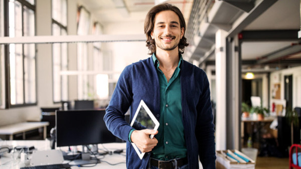 Portrait of smiling young handsome businessman standing with digital tablet at creative office