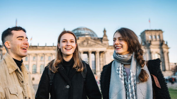 En grupp om tre personer pratar glatt framför Riksdagshuset i Berlin - efter kurs i tyska