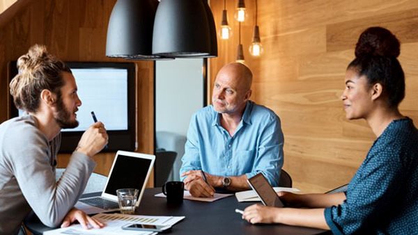 Tre deltagare sitter runt ett bord och diskuterar marknadsföring
