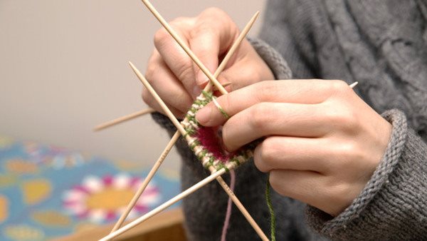 Närbild på händer som stickar med strumpstickor i flerfärgat garn - på kurs i handarbete